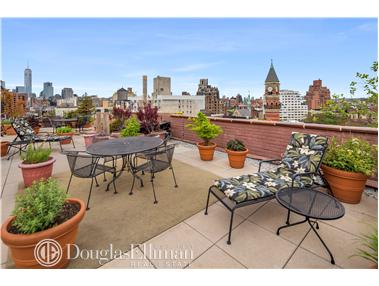 Rooftop patio with seating and potted plants, overlooking city skyline.