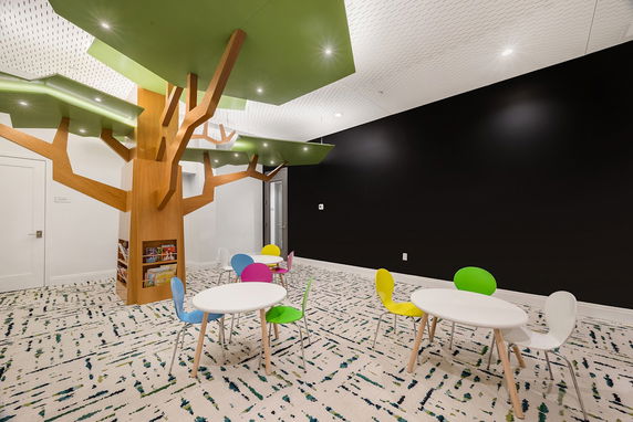 Colorful indoor play area with tree-shaped decorations and round tables with chairs.