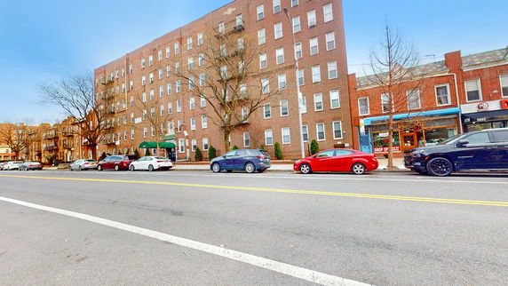 Front view of a multi-story brick building with parked cars on the street.