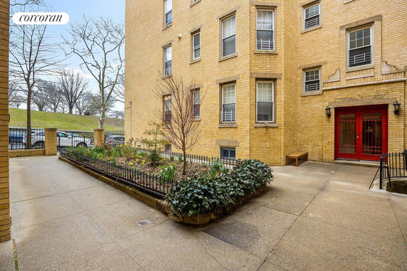 Front view of a brick apartment building with red door and garden.