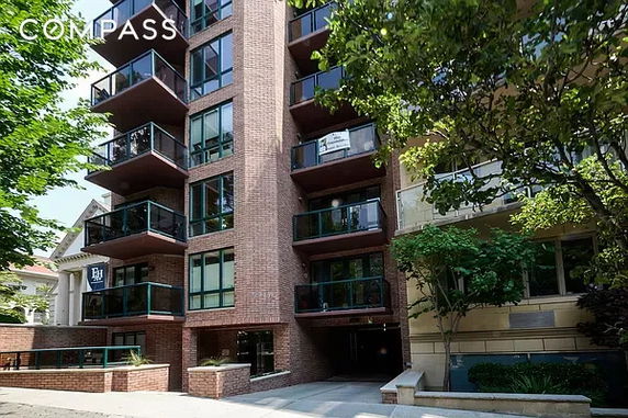 Front view of a multi-story brick apartment building with balconies and a glass entrance.