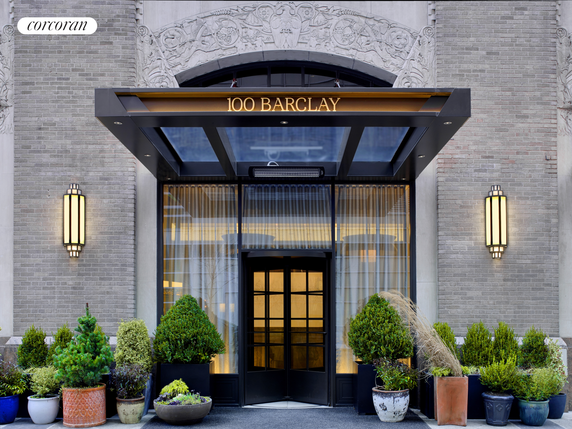 Front view of a building entrance with glass doors and decorative plants.