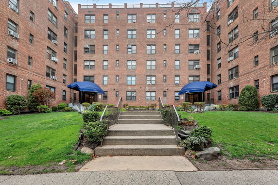 Front view of a multi-story brick apartment building with blue awnings over entrances.