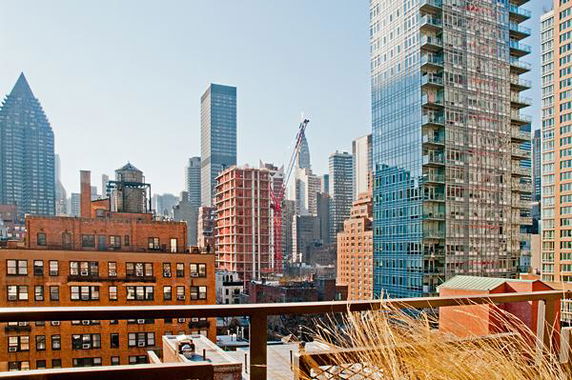 Panoramic view of city skyline with tall buildings and construction crane seen from a rooftop.