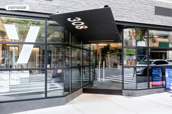 Front view of a modern building entrance with glass walls and a canopy with the number 308.