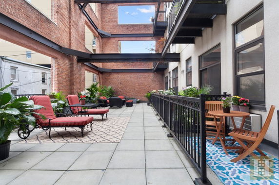 Outdoor rooftop terrace with lounge chairs, tables, and plants.