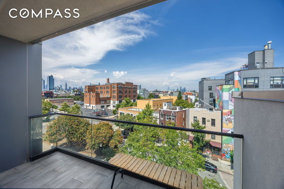 Panoramic city view from a building balcony with glass railing.