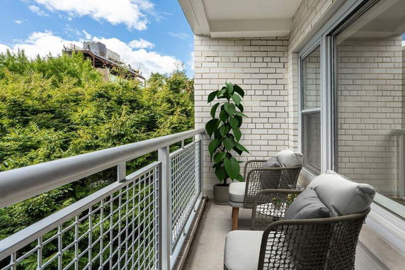 Balcony view with outdoor seating and greenery, showing a building with rooftop features in the background.