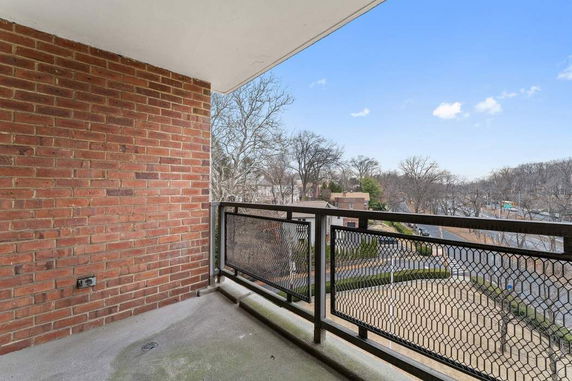 View from a balcony with a metal railing, overlooking a street and trees.