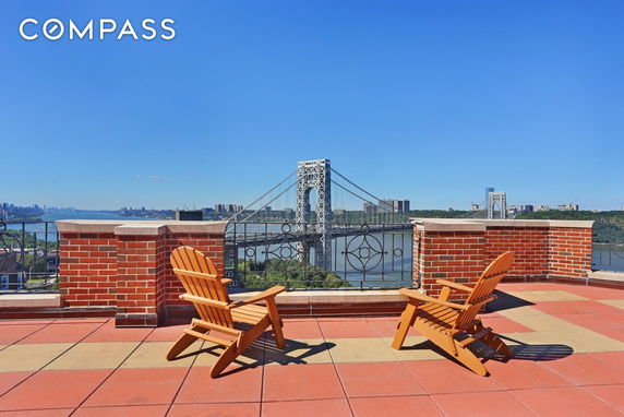 Rooftop view with chairs and a brick railing overlooking a bridge and river.