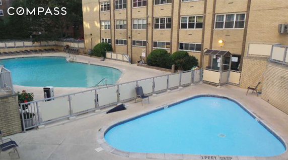 Outdoor swimming pool area adjacent to a multi-story brick building.