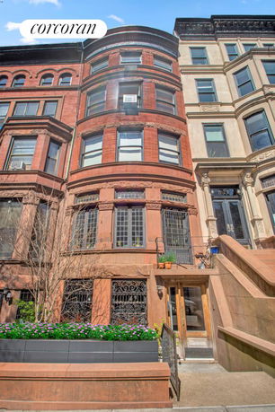 Front view of a multi-story brownstone building with ornate windows and a staircase leading to the entrance.