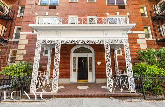 Front view of a multi-story brick building with decorative white ironwork around the entrance.
