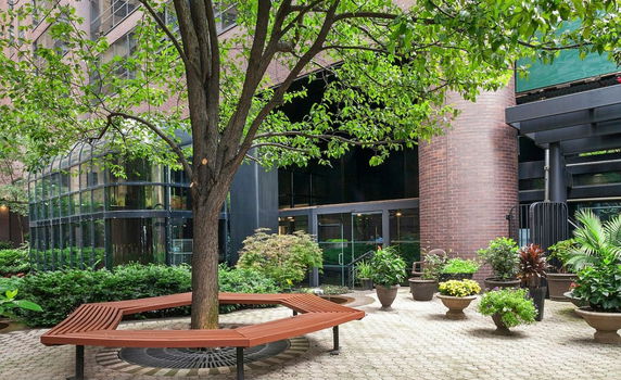 Front view of a building with glass windows and brick structure, featuring a tree and potted plants in the foreground.