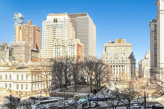 View of urban buildings with trees and people in a park setting.