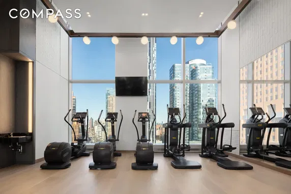 Gym area with exercise machines and large windows showcasing city views.