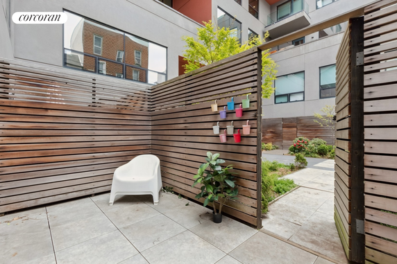 Courtyard view with a wooden privacy fence, potted plants, and a white chair.