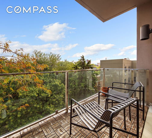 Balcony with metal chairs and glass railing overlooking trees and buildings.