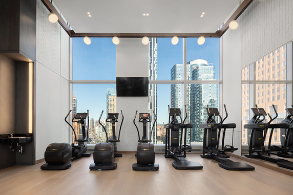 Indoor gym with exercise equipment and large windows.