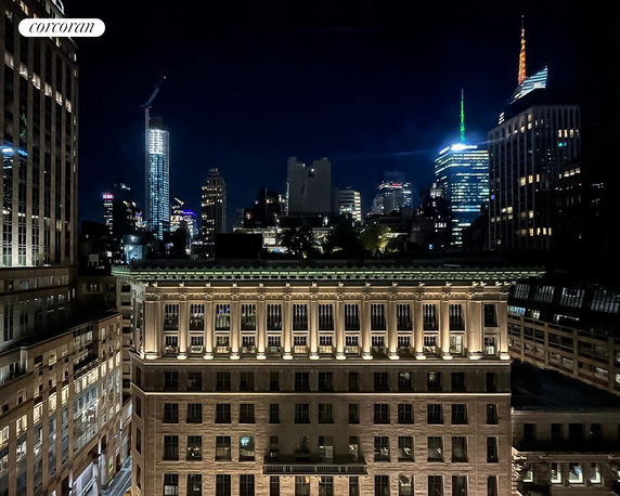 Nighttime cityscape view with illuminated buildings and skyscrapers in the background.