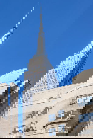 Front view of a tall skyscraper with a spire against a clear blue sky.