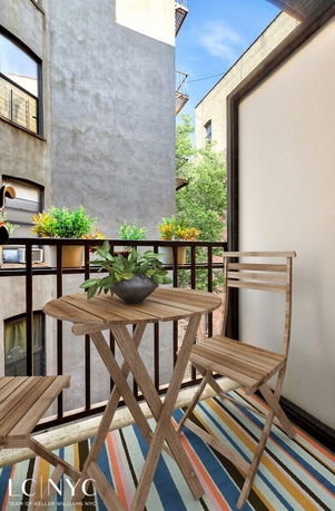Small outdoor balcony with wooden furniture overlooking adjacent buildings.