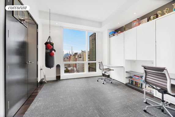 Room with punching bag, skateboards, and office chairs facing a window with city view.