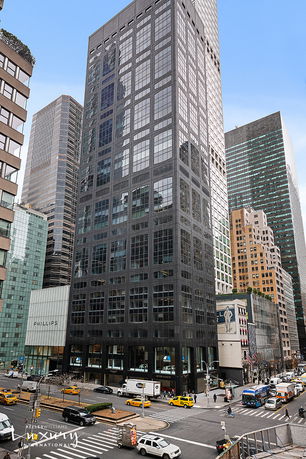 Front view of a tall, modern office building with glass windows on a busy city street.