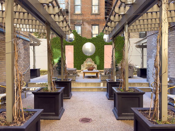 Outdoor area with trellises and planters, featuring a decorative wall with a circular mirror.