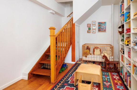 Room with wooden stairs, a crib, toys, and colorful rugs.