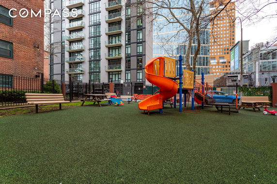 Outdoor playground area with climbing structure and slide surrounded by residential buildings.