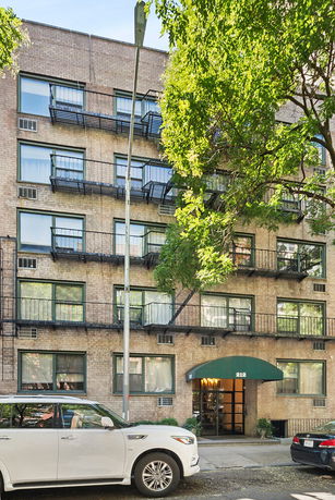 Front view of a multi-story apartment building with fire escapes and a canopy entrance.