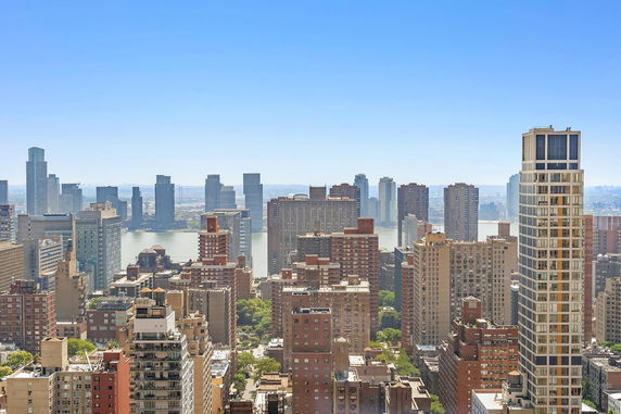 Panoramic view of a cityscape with numerous high-rise buildings and a river in the background.