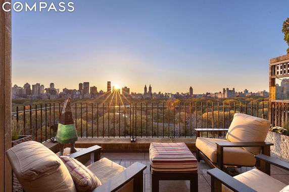 Panoramic view of a city skyline and park as seen from a terrace with chairs and table.