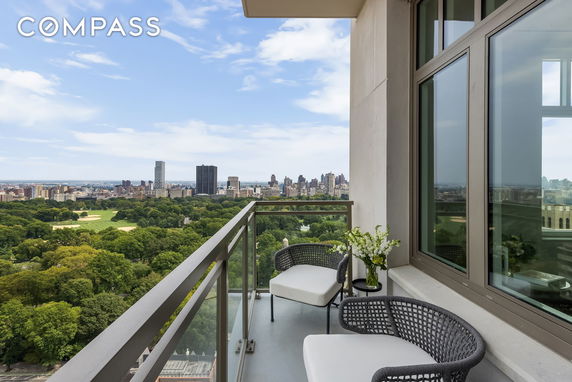 View from a balcony overlooking a large park and city skyline in the distance.