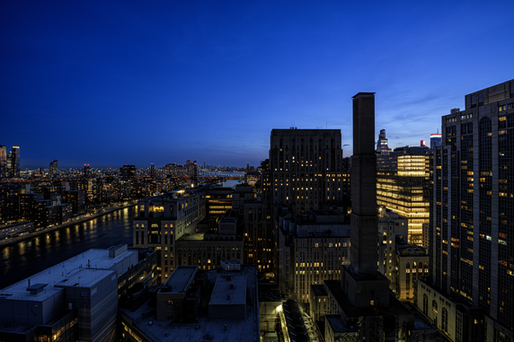 Panoramic view of a city skyline at dusk with illuminated buildings and a river.