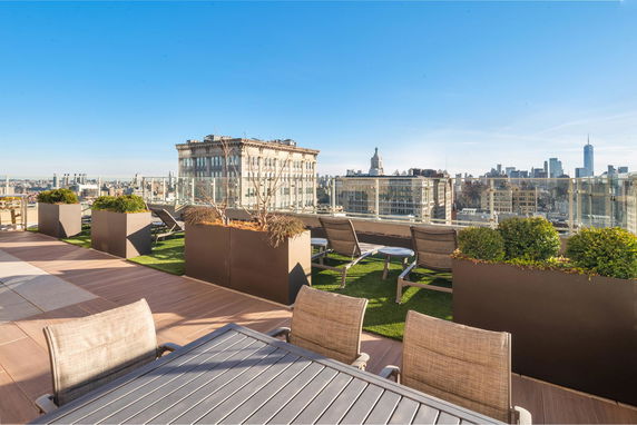 Rooftop with seating area and planters, city skyline visible in the background.