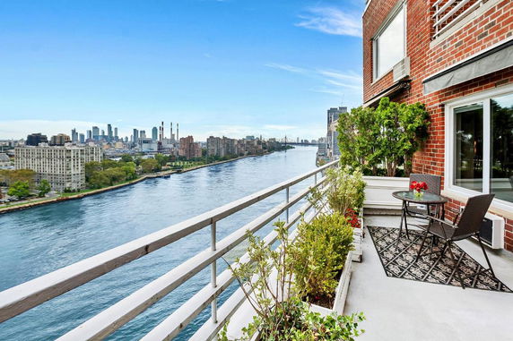 Balcony view of a river and cityscape with a brick building wall on the right.