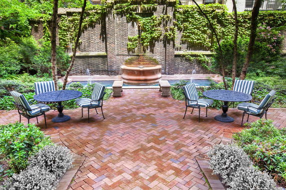 Patio area with metal tables and striped cushioned chairs, surrounded by greenery and a brick wall.