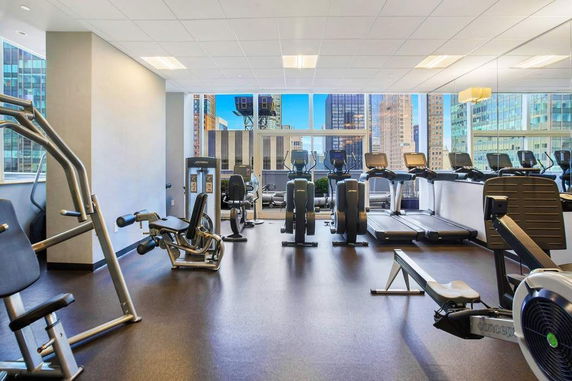 Indoor gym with various exercise machines and a view of city buildings through large windows.