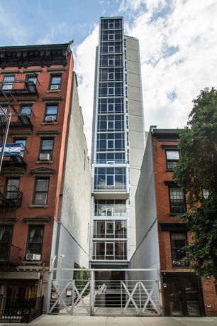 Front view of a tall, narrow modern building with glass windows, situated between older brick buildings.