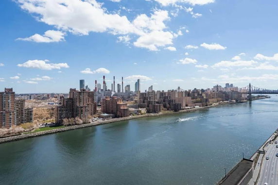 Panoramic view of a cityscape with high-rise buildings, a river, and a bridge visible.
