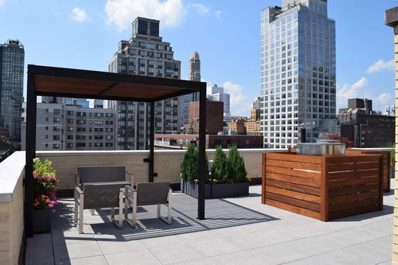 Rooftop terrace with seating area and planters, surrounded by cityscape buildings.