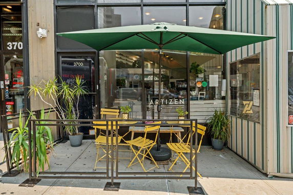 Front view of a cafe with outdoor seating and a green umbrella.