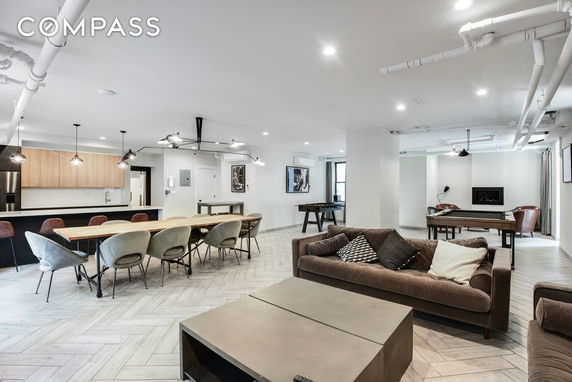 Interior view of a clubhouse with a large dining table, kitchen area, and seating arrangements.