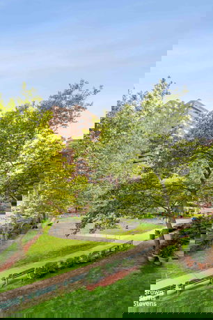 View of surrounding area showing a tall apartment building behind trees and a park with walkways and benches.