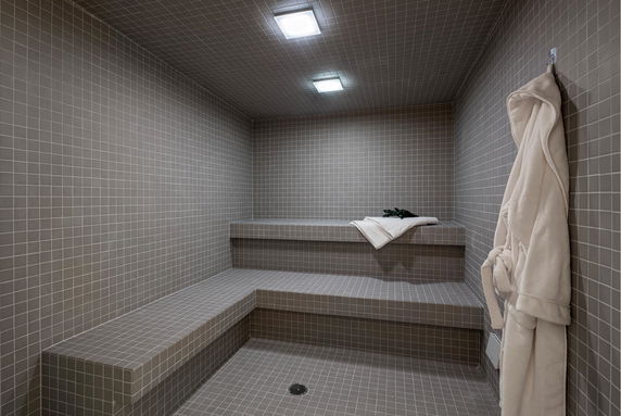 Interior view of a tiled steam room with benches and a robe hanging on the wall.