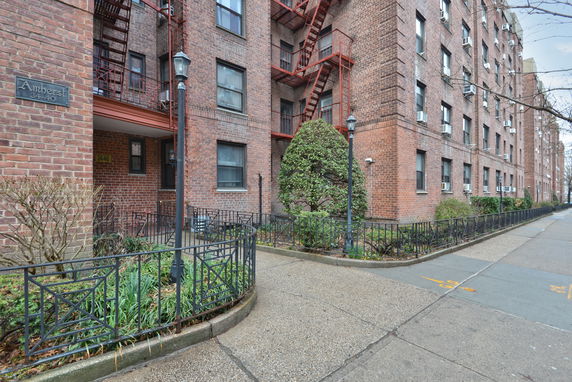 Front view of a multi-story brick apartment building with fire escapes and a small garden.