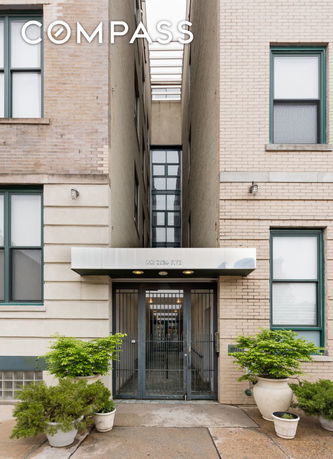 Front view of a building entrance with a gated door and decorative plants.