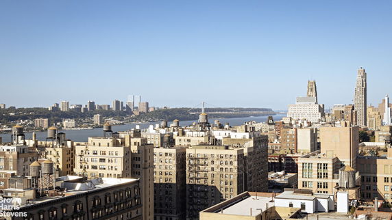 Panoramic view of urban skyline featuring multiple high-rise buildings and a distant bridge over a large body of water.